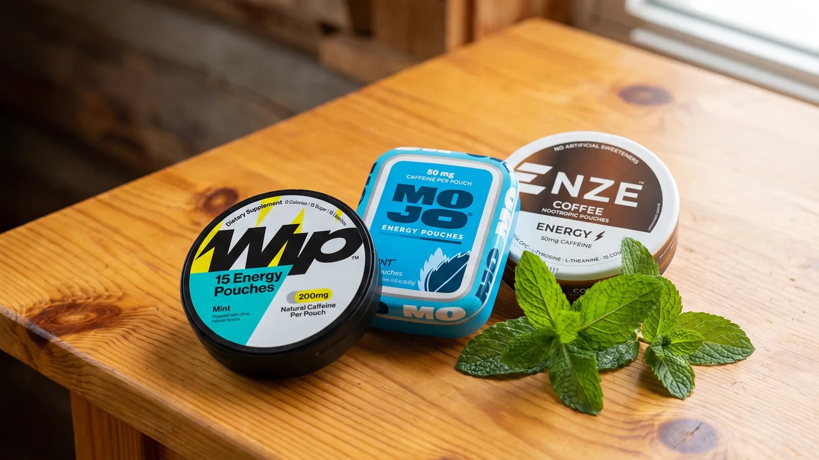 Wip, MOJO and NZE caffeine pouch tins with mint on a wooden table