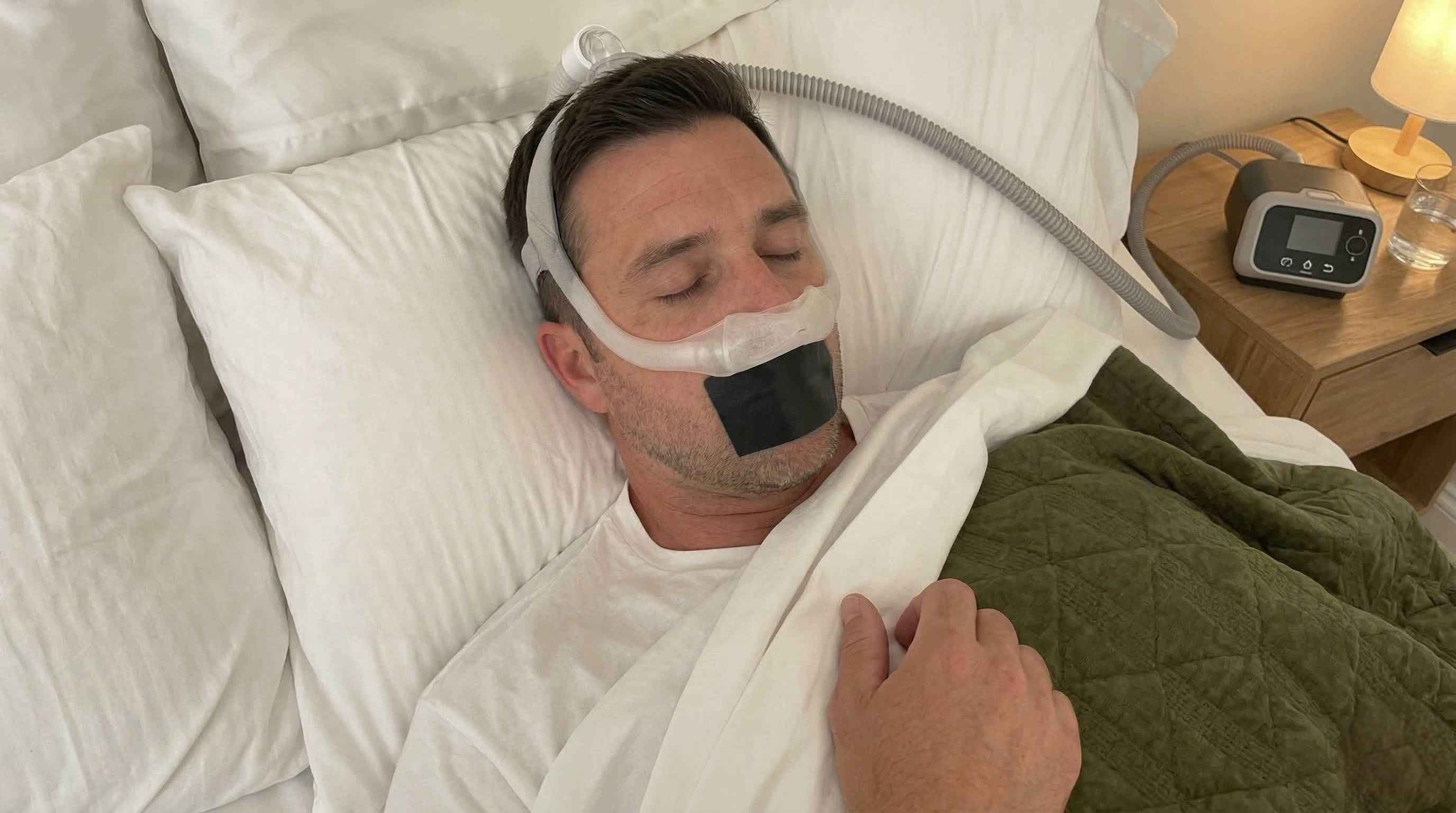 Person sleeping peacefully wearing nasal CPAP mask with mouth tape